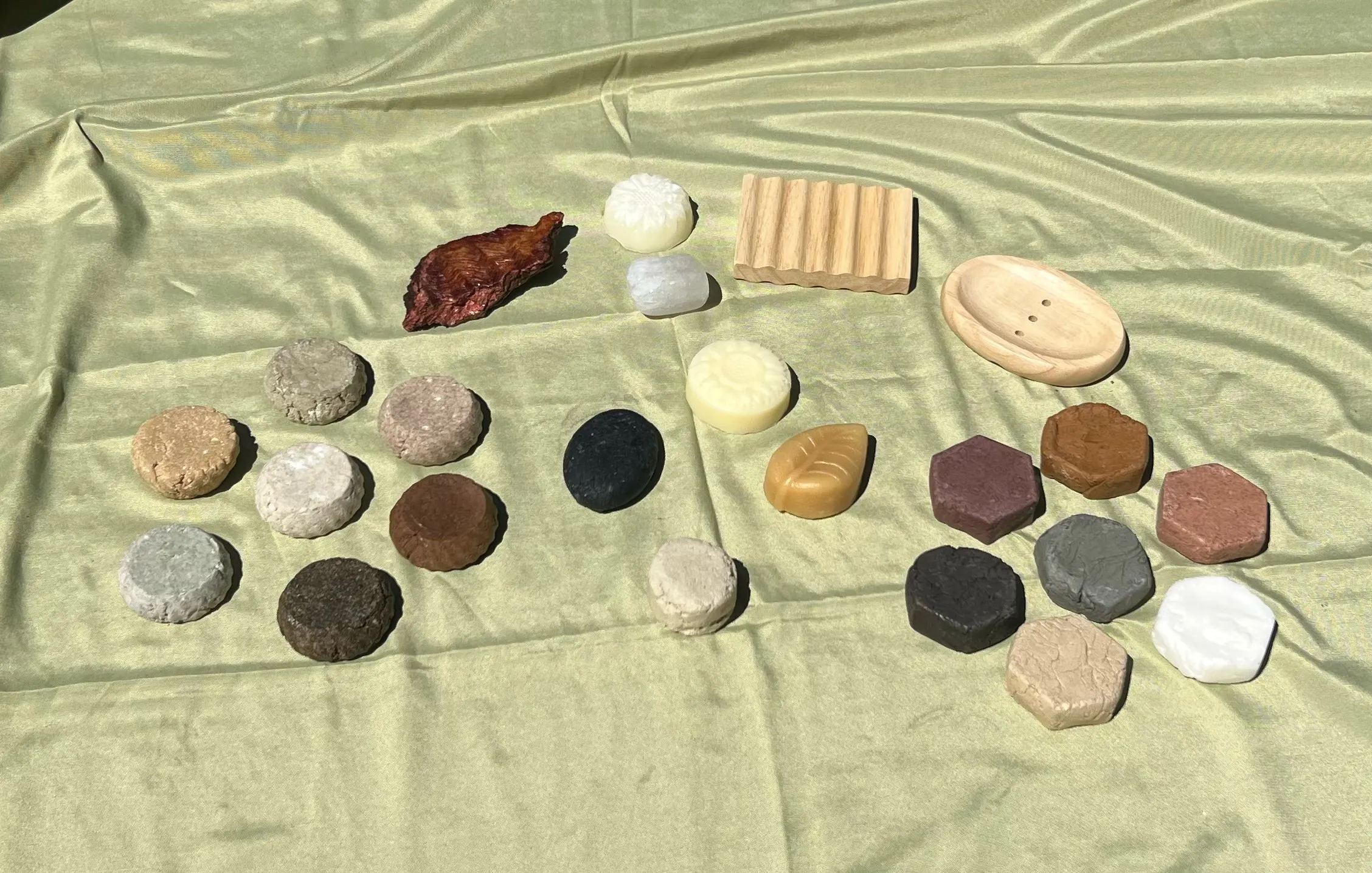 The full range of bars, soaps and beechwood dishes laid out on sage-green linen